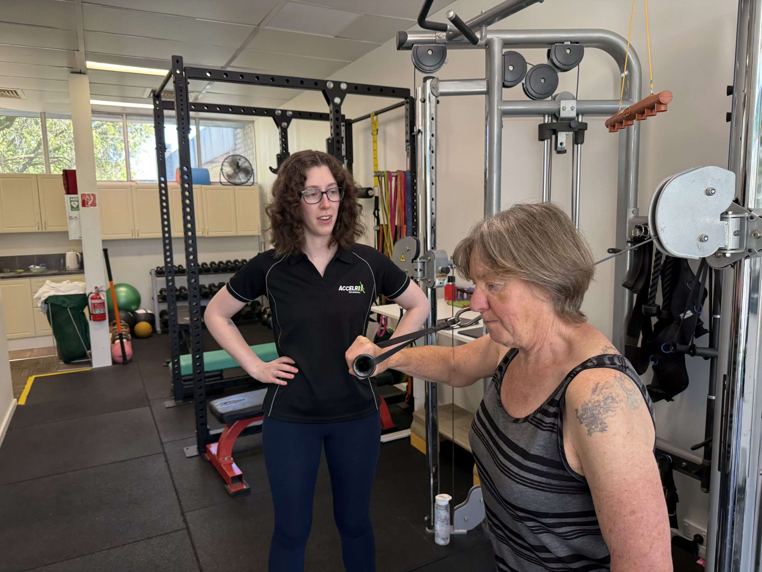 Exercise Physiologist Jess coaching a client on the cable machine in the Accelr8 Rehab clinic gym, Weetangera Canberra